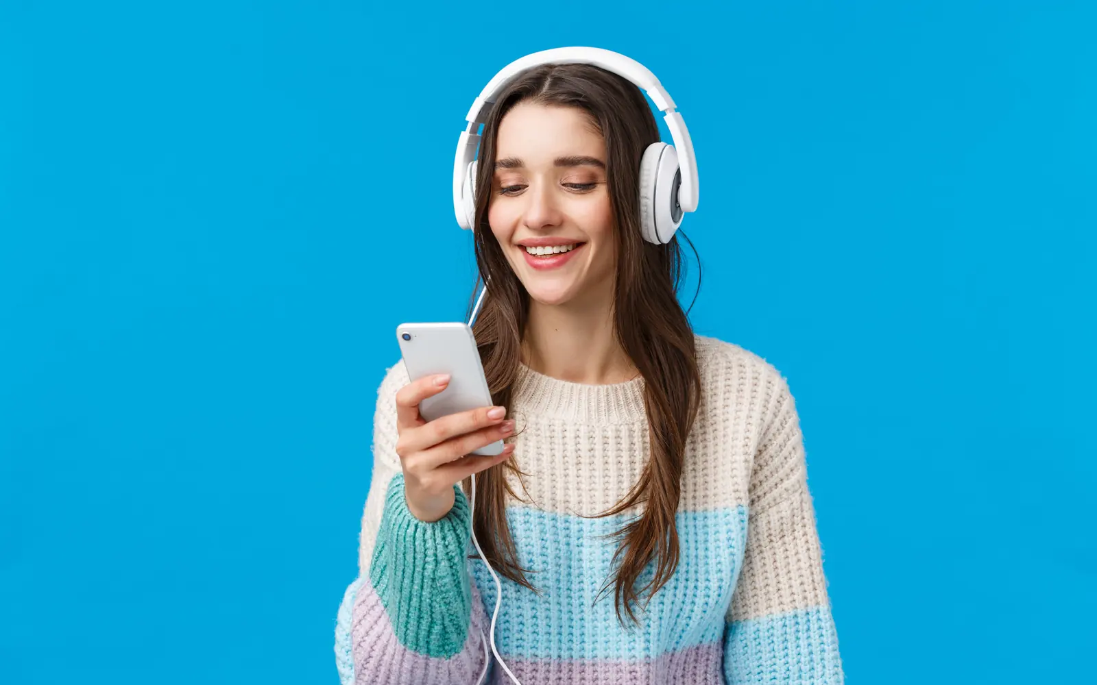 Una ragazza con le cuffie sorride guardando il telefono